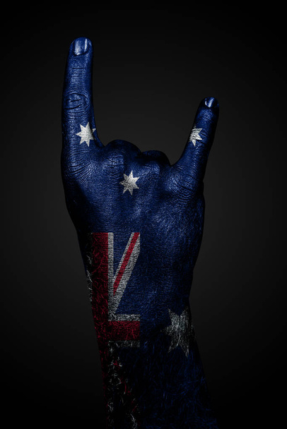 Una mano con una bandiera australiana disegnata mostra un segno di capra su uno sfondo scuro
. - Foto, immagini