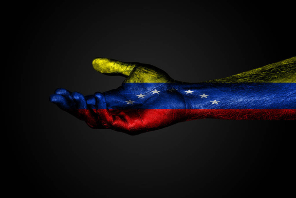 Протянутая рука с раскрашенным флагом Венесуэлы, знаком помощи или просьбой, на темном фоне
. - Фото, изображение
