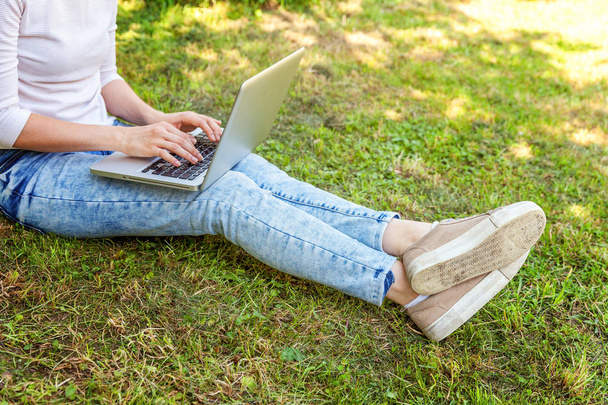 Kobieta nogi na Zielona trawa trawnik w parku miejskim, rąk do pracy na komputerze pc laptop. Koncepcja działalności freelancerskiej - Zdjęcie, obraz