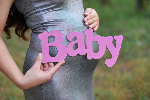 zwanger meisje met buik wachten met letters inscriptie brief roze in haar handen in een park buitenshuis - Foto, afbeelding