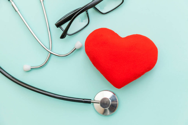 Ιατρικό εξοπλισμό στηθοσκόπιο ή φωνηνολογικό γυαλιά και κόκκινη καρδιά απομονώνεται σε μοντέρνο παστέλ μπλε φόντο. Συσκευή οργάνου για το γιατρό. Έννοια της ασφάλισης ζωής στην υγειονομική περίθαλψη - Φωτογραφία, εικόνα