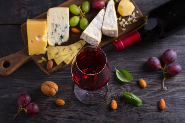 Glass and bottle of wine with cheese, grapes, and nuts on black wooden table. Wine and food. View from above, top studio shot - Fotoğraf, Görsel