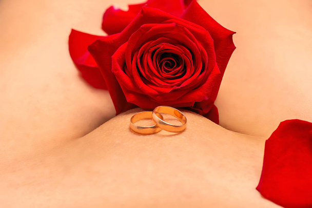 The concept of preserving virginity before the wedding. Outdated values, morals, restrictions, religious foundations. Depilated female body, wedding rings and red rose - Photo, Image