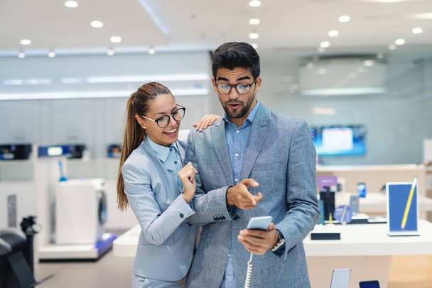 Carino multiculturale coppia vestita elegante scegliendo nuovo smartphone nel negozio di tecnologia. Uomo che punta al telefono intelligente
. - Foto, immagini