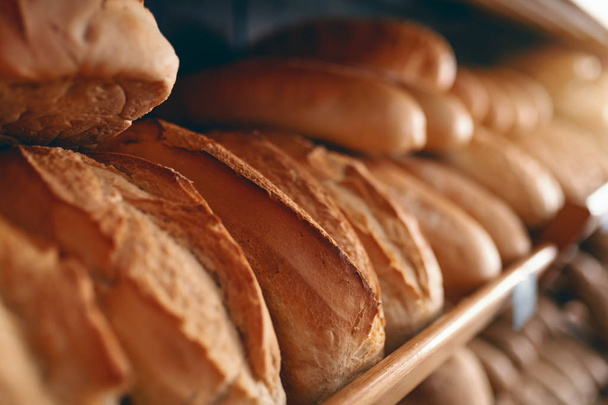 Close up of fresh delicious loafs of bread in row on shelves ready for sale. Bakery interior. - Foto, immagini