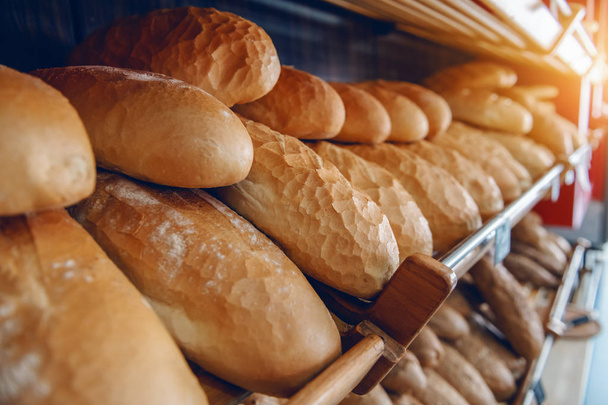 frische, köstliche Brotlaibe in Reih und Glied in Regalen, die zum Verkauf bereit stehen. Bäckereiinnenraum. - Foto, Bild