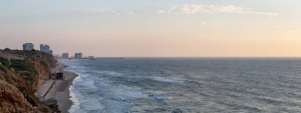 Piękny panoramiczny widok na wybrzeżu Oceanu, w którym panuje tętniący życiem zachód słońca przy plaży Apollonia. Podjęte w Herclijja, Dystrykt Tel Aviv, Izrael. - Zdjęcie, obraz