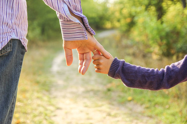 der Elternteil hält die Hand des Kindes mit einem glücklichen Hintergrund - Foto, Bild