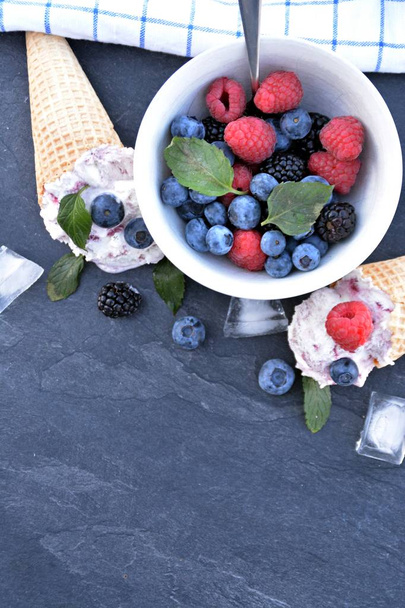  Waffle fagylalt kúp töltött erdei gyümölcs fagylalt labdák, friss bogyós gyümölcsök és a menta feküdt egy sötét márvány felület-koncepció egy hűvös nyári kaland, finom gyümölcsös fagylalttal - Fotó, kép