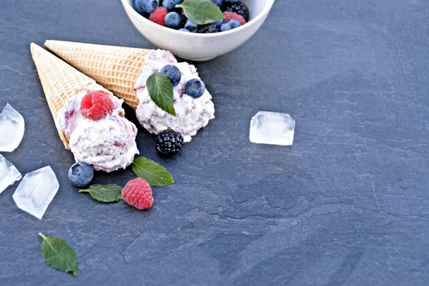  вафельні конуси морозива, наповнені лісовими фруктовими морозивами зі свіжими ягодами та м'ятою, лежать на темній мармуровій поверхні концепція прохолодної літньої пригоди зі смачним фруктовим морозивом
 - Фото, зображення