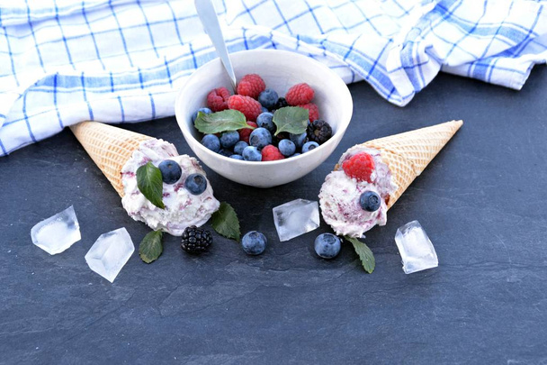  Waffle fagylalt kúp töltött erdei gyümölcs fagylalt labdák, friss bogyós gyümölcsök és a menta feküdt egy sötét márvány felület-koncepció egy hűvös nyári kaland, finom gyümölcsös fagylalttal - Fotó, kép