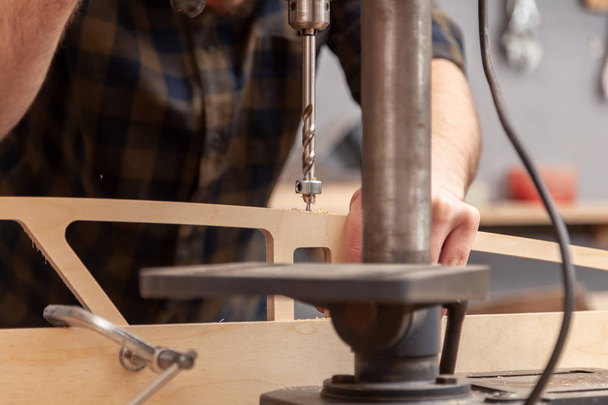 Homem de carpinteiro em roupas de trabalho faz um buraco no produto de madeira com uma broca elétrica.Conceito de fazer-você-mesmo trabalho masculino com árvore e construção de casa
 - Foto, Imagem