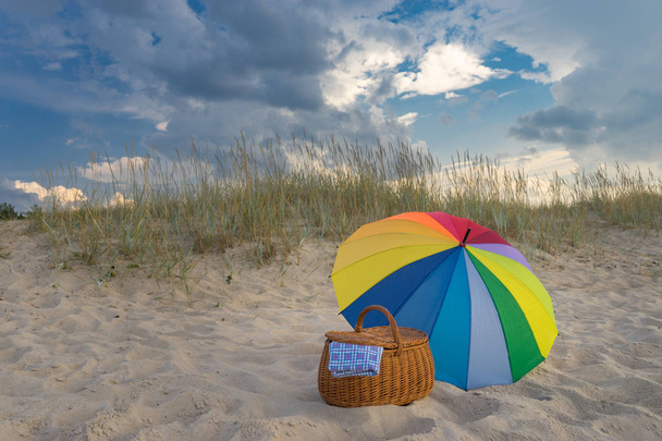Ombrellone e cestino da picnic contro spiaggia e nuvole
 - Foto, immagini