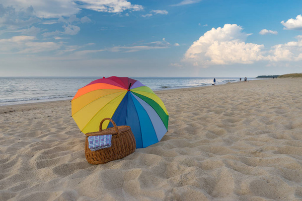 Ομπρέλα και καλάθι πικνίκ κατά της θαλάσσιας ακτής - Φωτογραφία, εικόνα