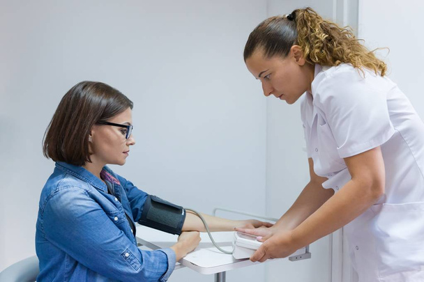 Nurse taking female patient's blood pressure in office - Foto, Bild