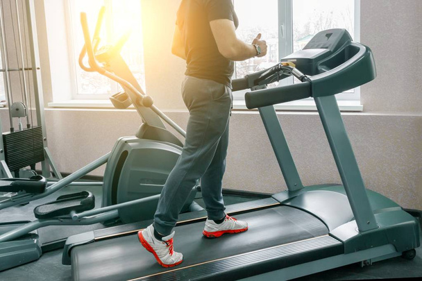 Athletic muscular man running on treadmills in modern sport gym. Fitness, sport, training, people concept. - 写真・画像