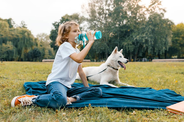 Little girl with white dog Husky in the park sits on the grass, plays, reads, resting - Фото, изображение