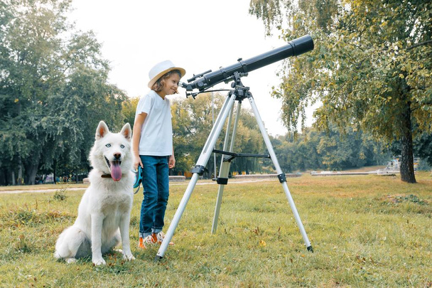 Girl child with a white dog husky with interest looking through a telescope at the sky - Zdjęcie, obraz
