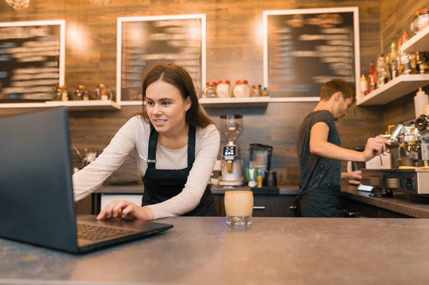 Team of coffee shop workers working near the counter with laptop computer and making coffee, cafe business - Valokuva, kuva