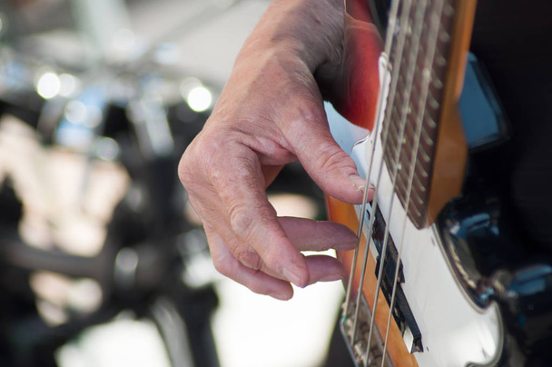 closeup of hand of musician on bass guitar in outdoor - Фото, изображение