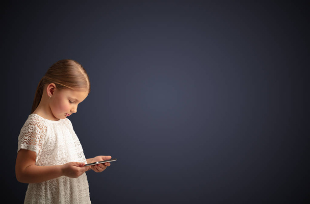 Cute little girl using tablet with dark background - Zdjęcie, obraz