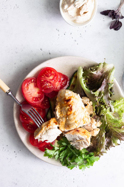 Opékací kuřecí prsa (řízek) se smetanovou omáčkou na talíři se zeleným salátem, rajčaty a grilovanou cuketou. - Fotografie, Obrázek