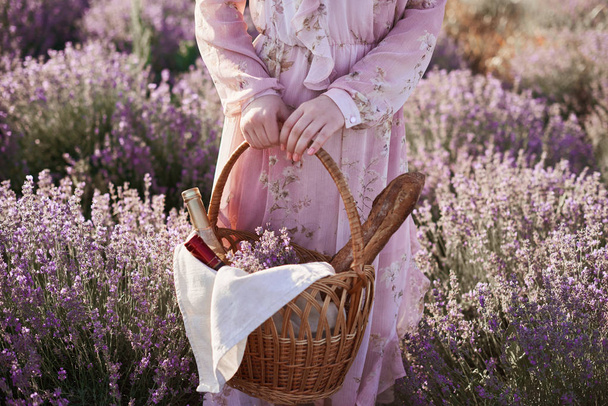 lány a romantikus ruhát fonott kosár bor és a kenyér a kezében keresi a jó hely a piknik - Fotó, kép