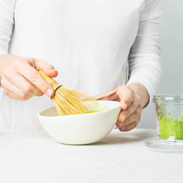 Woman preparing green Matcha tea in white bowl with bamboo Chasen whisk on white background - Valokuva, kuva