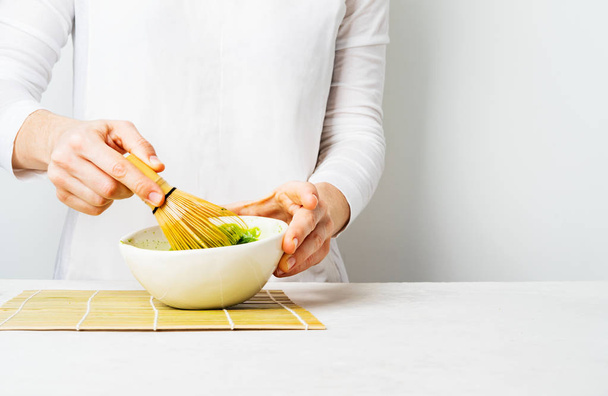 Woman preparing green Matcha tea in white bowl with bamboo Chasen whisk on white background - Foto, afbeelding