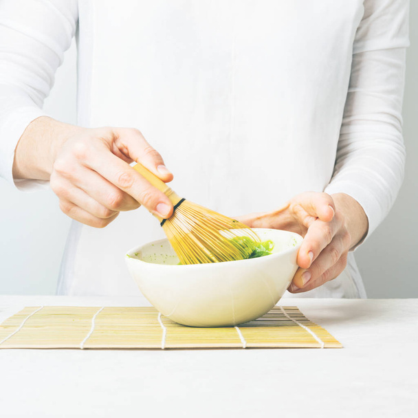 Woman preparing green Matcha tea in white bowl with bamboo Chasen whisk on white background - 写真・画像