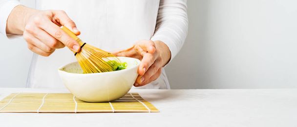 Woman preparing green Matcha tea in white bowl with bamboo Chasen whisk on white background - Φωτογραφία, εικόνα