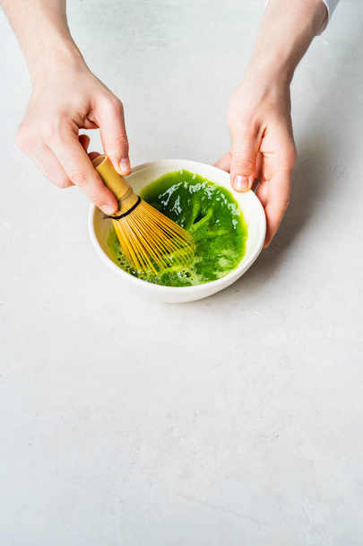 Woman preparing green Matcha tea in white bowl with bamboo Chasen whisk on white background - Fotoğraf, Görsel
