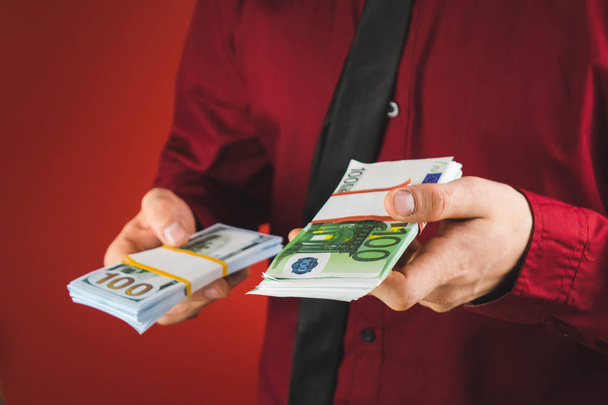 Человек в красной рубашке с карточкой держит в руке пачку банкнот на красном фоне
 - Фото, изображение