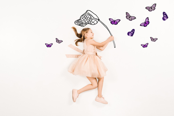 Draufsicht von fröhlichem Kind im rosa Kleid mit Schmetterlingsnetz in der Nähe von Schmetterlingen auf weißem Grund  - Foto, Bild