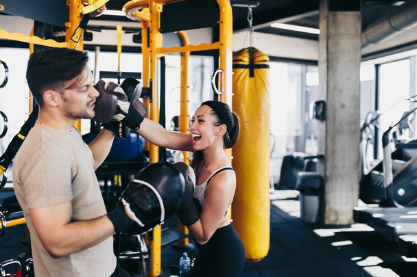 Young attractive woman with instructor on kickboxing training. She hitting or punching in big yellow boxing bag. - Foto, Imagen