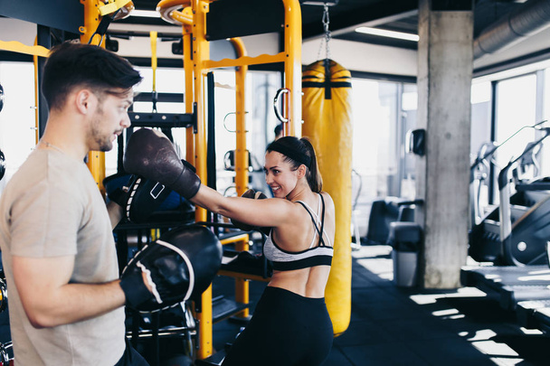 Young attractive woman with instructor on kickboxing training. She hitting or punching in big yellow boxing bag. - Foto, immagini