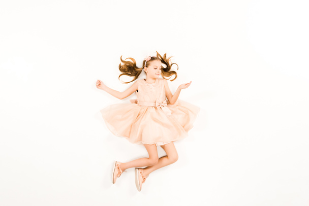 Blick von oben auf ein glückliches Kind im rosa Kleid, das lächelt, während es weiß fliegt - Foto, Bild