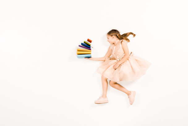 top view of cheerful kid in pink dress holding books on white - Фото, зображення