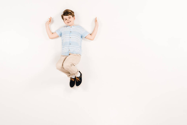 top view of happy kid looking at camera while lying on white  - Foto, imagen