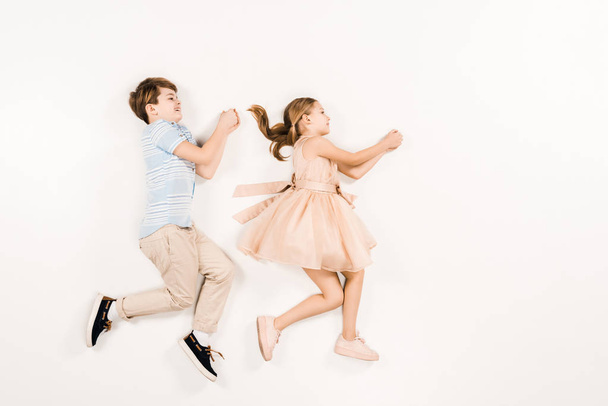 vista superior de niños alegres haciendo gestos mientras están acostados en blanco
  - Foto, Imagen