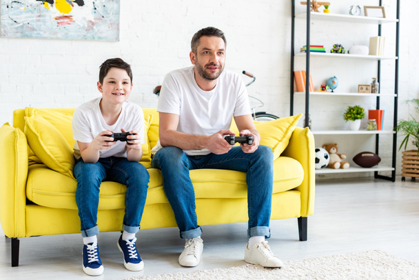 father and son playing Video Game on couch in Living Room - Fotografie, Obrázek