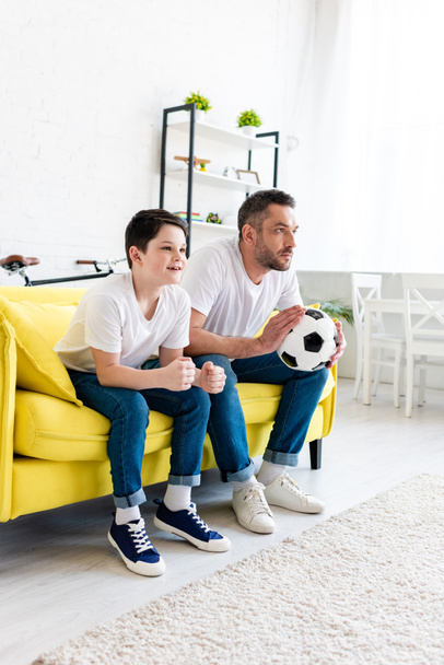 father and son watching sports match on couch at home - Foto, Bild