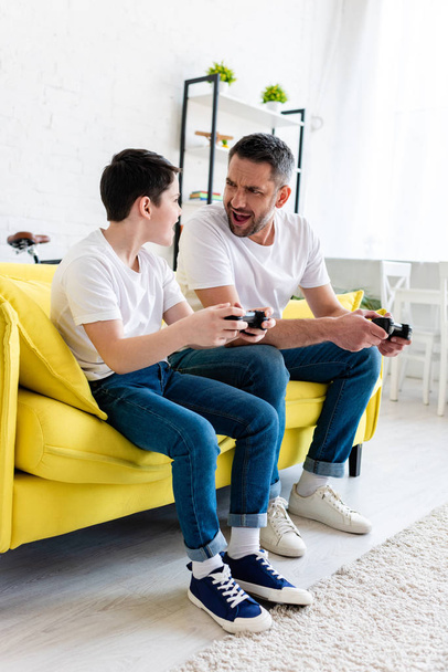 izgatott apa és fia játszik Video Game ülve heverő nappaliban - Fotó, kép