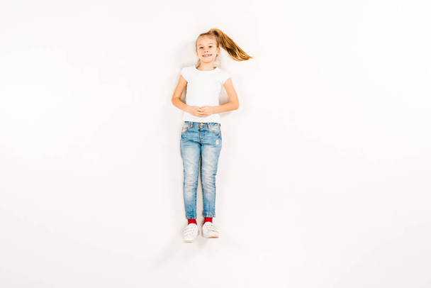 top view of happy kid with clenched hands lying on white  - Photo, Image