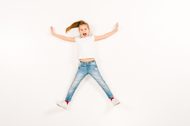 top view of scared kid screaming while lying on white  - Fotografie, Obrázek