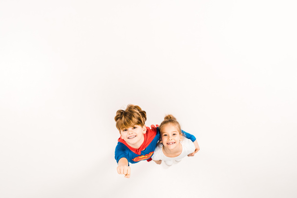 スーパーヒーローの衣装で幸せな子供のトップビューは、友人を抱きしめ、白にジェスチャー  - 写真・画像