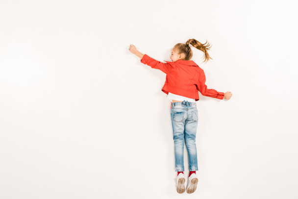 top view of happy kid in blue jeans gesturing while lying on white  - Foto, immagini