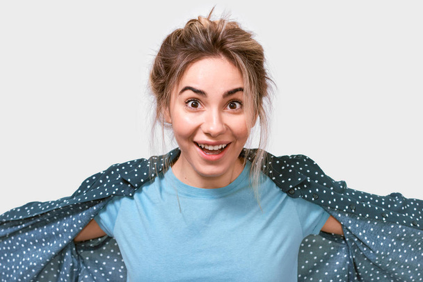 Happy surprised young beautiful woman in blue t-shirt, smiling broadly, looking cheerful and excited to the camera, posing on white studio background. Real human emotions. - Photo, Image