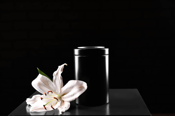 Mortuary urn with lily flower on table against dark background - Fotó, kép