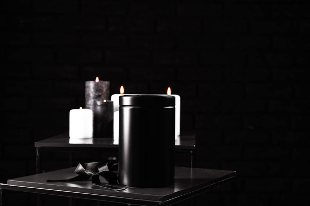 Urne mit Schleife auf Tisch vor dunklem Hintergrund - Foto, Bild
